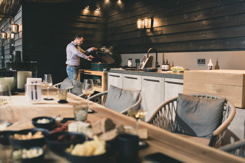 A man tending to his smoker next to a dark walled house