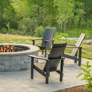 A photo of black adirondack chairs in front of a stone fire table.