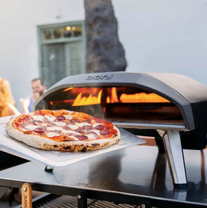 Photo of fresh pizza in front of a portable pizza oven.