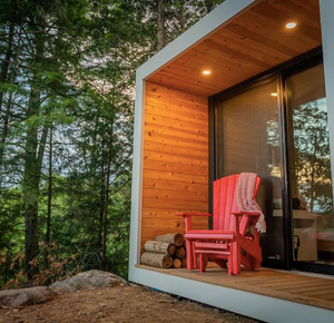 a photo of a red adirondack chair on the front porch of a modern cabin.